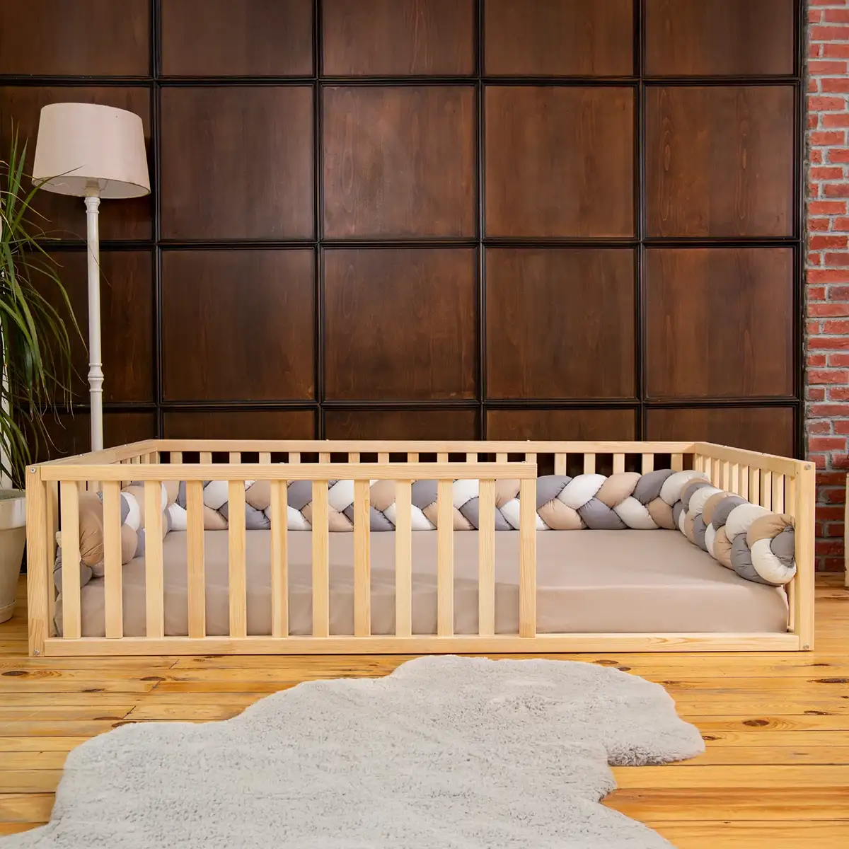 Wooden toddler bed with decorative bumper pad in a room with wooden walls and a lamp.